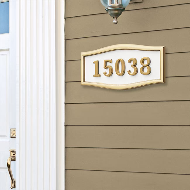 A house number address sign reading 15038 in gold numerals with a white background and gold frame, mounted on a brown horizontal siding exterior wall.